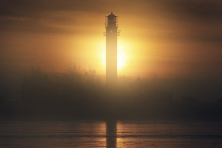 Lonely lighthouse and a frozen seashore at sunset. Atmospheric winter landscape. Warm golden sunlight, setting sun. Picturesque scenery. Travel destinations, navigation, symbol of hope and peaceの写真素材