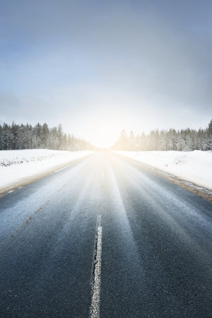 An empty clean highway through the snow-covered fields and coniferous forest after a blizzard. Dramatic sky with glowing clouds. Karelia, Russia. Dangerous driving, road trip conceptsの写真素材
