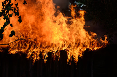 Ruins of the wooden country house and fence in a flame. Fire and smoke textures close-up. Forest fires in summer. Seasons, ecology, ecological issue, environmental damage, disaster, danger conceptsの写真素材