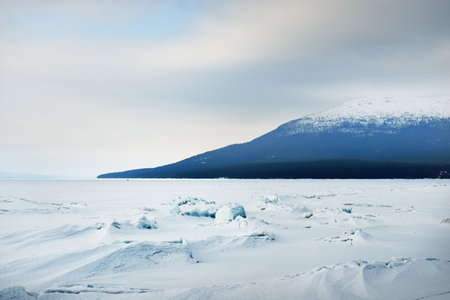 Ice pressure ridge on a frozen lake shore. Mountain peaks in the background. Dramatic cloudscape. Picturesque winter scenery. Ecology, environment, climate change, global warming concepts. Canadaの写真素材