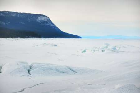 Ice pressure ridge on a frozen lake shore. Mountain peaks in the background. Dramatic cloudscape. Picturesque winter scenery. Ecology, environment, climate change, global warming concepts. Canadaの写真素材