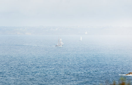 Two-masted gaff schooner (tall ship) and modern white yacht near the rocky shores of Brittany, France. Travel, history, transportation, sailing, sport, cruise, regatta. Panoramic aerial viewの写真素材