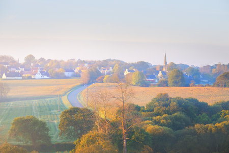 Trees, valley, old cathedral, houses and empty highway in a fog at sunrise. Panoramic aerial view, cityscape. Soft morning light. Picturesque scenery. Vacations in Brittany, France. Travel, tourismの写真素材