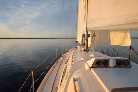 White yacht sailing after the rain at sunset. Close-up view from the deck to the bow. Clear blue sky...