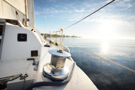 White yacht sailing after the rain. Close-up of the mast winch. Clear blue sky and clouds reflecting...