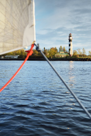 Lighthouse, range marker and breakwaters at sunset. Baltic sea, Latvia. Idyllic landscape. A view from the yacht, white sail close-up. Transportation, sailing, navigation. Symbol of hope and peaceの写真素材