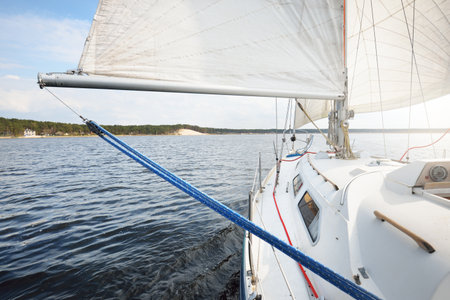 White yacht with full sails running downwind wing-on-wing, sailing after the storm. Close-up view...