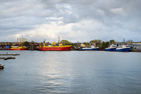 Small ship (boat) moored to a pier in the fishing harbor at sunset. Ventspils, Latvia. Farm and food industry, traditional craft, freight transportation, logistics, environmental damage conceptsの写真素材