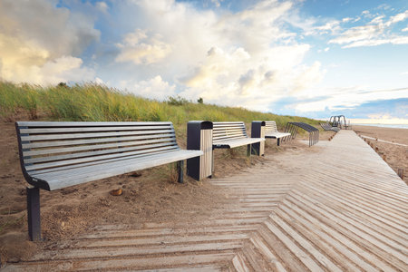 An empty modern wooden promenade through the sandy shore of the Baltic sea, bench close-up. Sport, recreation, cycling, nordic walking, relaxation, vacations, weekend, tourism, leisure activityの写真素材