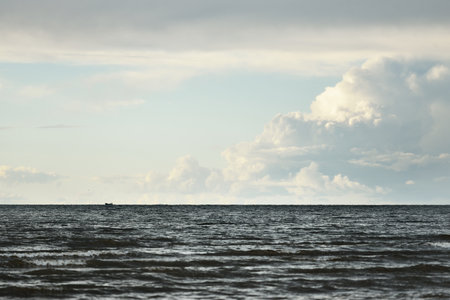 Clear sky with lots of white glowing cumulus clouds above the Baltic sea shore after thunderstorm at sunset. Dramatic cloudscape. Warm golden light. Picturesque scenery. Fickle weather, climate changeの写真素材