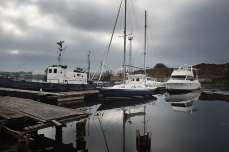 Old tugboat, elegant and modern sailboats moored to a pier in a yacht marina, close-up. Storm sky....