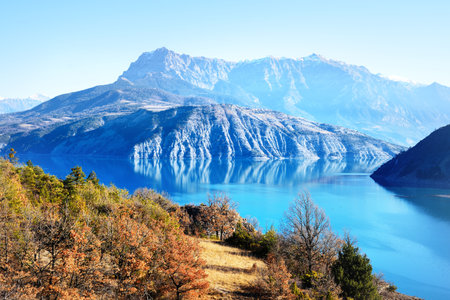 Panoramic view of the mountain lake Lac de serre-poncon in French Alps on a sunny day. Clear blue sky, still water. Travel destinations, tourism, landmark, nature, Christmas vacations in Franceの写真素材