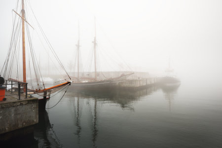 Vintage wooden yachts and fishing boats moored to a pier, close-up. Heavy morning fog. Germaniahafen, Kiel, Germanyの写真素材