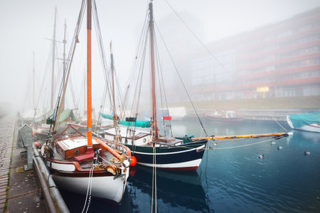 Vintage wooden yachts and fishing boats moored to a pier, close-up. Heavy morning fog. Germaniahafen, Kiel, Germanyの写真素材