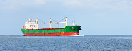 Large green cargo crane ship sailing in an open sea under dramatic blue sky. Epic seascape. Freight transportation, global communications, delivering, fuel and power generation, industry, logisticsの写真素材