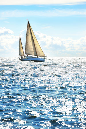 Vintage white wooden sailing boat sails in an open sea on a cloudy dayの写真素材