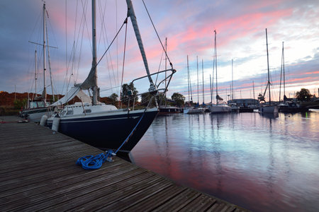 Blue sloop rigged yacht close-up. Sailing boats moored to a pier at sunset. Dramatic evening sky...