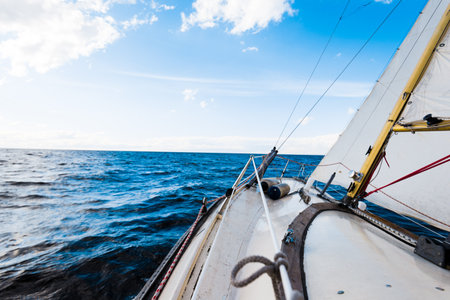 Sloop rigged yacht sailing on a clear day. A view from the deck to the bow and sails. Waves and water splashes. Baltic sea, Latviaの写真素材