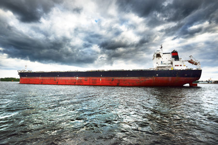 Large black cargo ship, close-up. Dark storm sky. Port of Riga in the background. Baltic sea, Latviaの写真素材