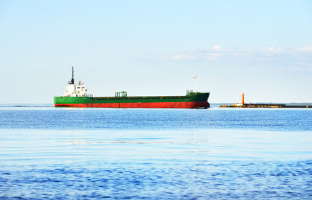 Large cargo ship sailing in the Baltic sea on a clear sunny day. Lighthouse in the background. Latviaの写真素材