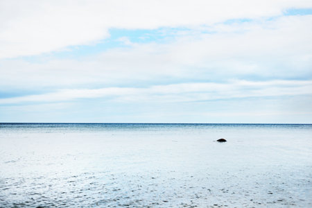 Cloudy blue sky above the Baltic sea. Lonely stone in the water. Ruhnu island, Estoniaの写真素材