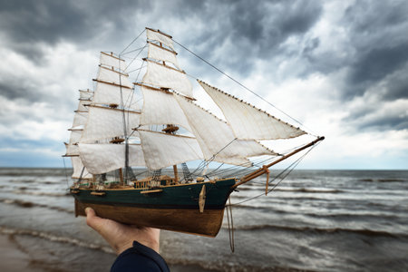 Antiquarian wooden scale model of the clipper tall ship, close-up. Dramatic sky, dark stormy clouds and sea. Traditional craft, souvenir, hobby, collecting, vintage, modeling. Zero waste conceptの写真素材