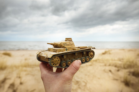 German WWII Panzer III scale model toy tank in a hand close-up. Sand dunes of the Baltic sea in the background. Modeling, collecting, education, history conceptsの写真素材