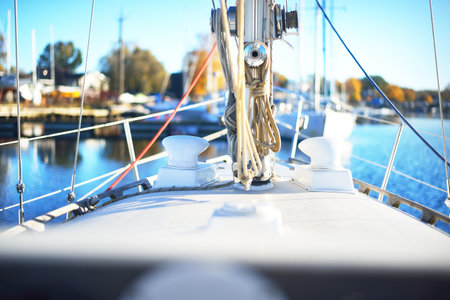 White sailboat moored to a pier in a yacht marina on a clear day. Close-up view from the deck to the bow, mast and rigging equipment. Vacations, sport, amateur recreational sailing, cruiseの写真素材
