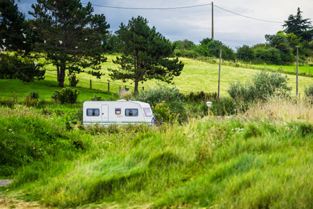 A caravan trailer with a bicycle parked in a green valley on a cloudy day. Forest in the background. Normandy, Franceの写真素材