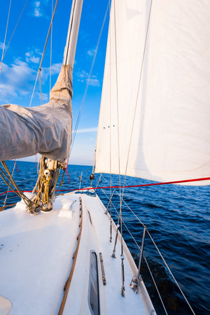 White yacht sailing in a still water at sunset. A view from the deck to the bow, mast and sails. Stunning cloudscape. Natural mirror. Sport and recreation theme. Baltic sea, Latviaの写真素材