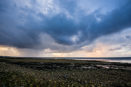 Rocky sea shore under dramatic stormy sunset sky. Mossy stones close-up. Shallow water. Epic cloudscape. English Channel, Normandy, Franceの写真素材