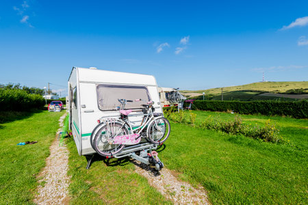 A caravan trailer with a bicycle parked in a green valley on a sunny day. Summer campsite. Normandy, France. Travel, leisure activity, recreation themeの写真素材