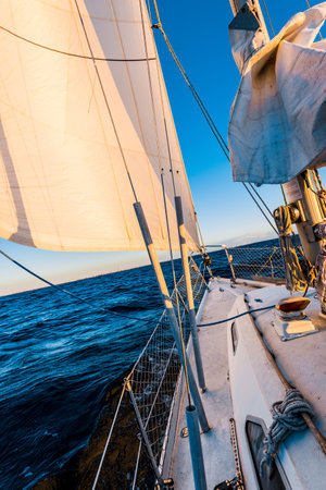 White yacht sailing at sunset. A view from the deck to the bow, mast and sails. Norway