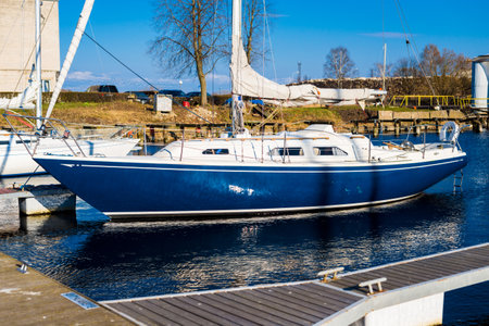 Blue sloop rigged yacht moored to a pier after winterization in winter. Clear blue sky. Port of...