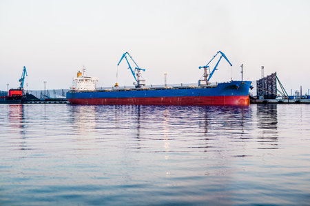 Cargo ship in the port of Riga, Latvia, at sunset. Port cranes in the background