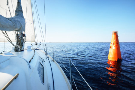 White yacht sailing on a clear sunny day. Close-up view from the deck to the bow and sails. Waves...