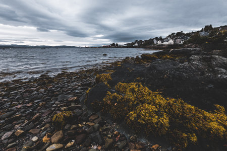 A view of the rocky shore of Crinan Canal. Houses in the background. Ardrishaig, Argyll and Bute, Scotland, UK. Dark dramatic sky. Travel destinations, tourism, sightseeing. sailing, cruiseの写真素材
