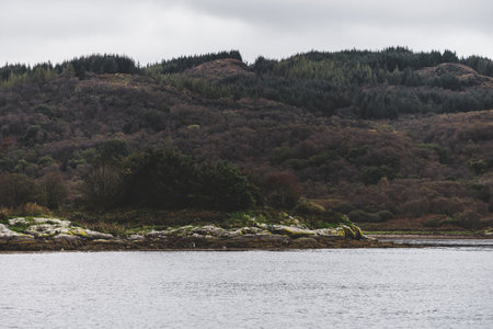 Sailing near the rocky shores of Kyles of Bute on a cloudy day. Scotland, UK. Dramatic stormy sky. Travel destinations, national landmarks, tourism, vacations, leisure activity conceptsの写真素材