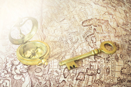 Retro styled golden antique compass (sundial) and a key on the old white nautical chart close-up. Vintage still life. Sailing accessories. Travel, navigation, collecting, souvenir, graphic resourceの写真素材