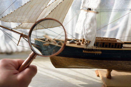 Retro copper colored magnifying glass (hand lens) and wooden tall ship scale model close-up. Vintage...