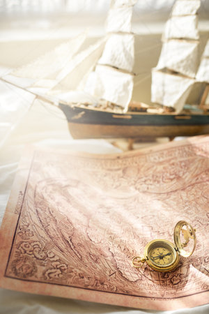Retro styled golden antique compass (sundial), wooden tall ship scale model and old white nautical...