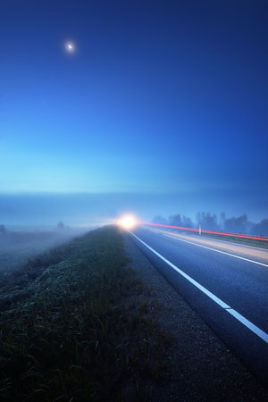 Panoramic view of the empty highway through the fields in a fog at night. Moonlight, clear sky. Sunrise. Europe. Transportation, logistics, travel, road trip, freedom, driving. Rural sceneの写真素材