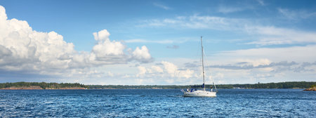 Small white sloop rigged yacht near the rocky Finland shoreline. Dramatic sky. Transportation,...
