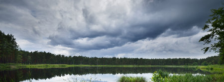 Dramatic sunset sky with glowing cumulus clouds above the lake and evergreen pine forest after the rain. Idyllic rural scene. Panoramic view. Vacations, ecotourism, nature, seasons. Scandinaviaの写真素材