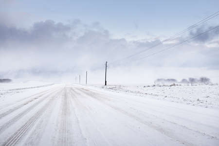 Snow-covered rural road through the field. Electricity line, transformer poles. Panoramic view from the car. Colorful clouds, dramatic sunset sky. Off-road, logistics, winter tires, remote villageの写真素材