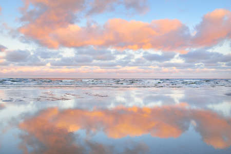 Panoramic view of the Baltic sea from a sandy shore. Clear sunset sky, colorful glowing pink clouds,...