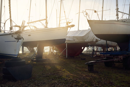 Winterized sloop rigged yacht standing on land, close-up. Waiting for the new sailing season. Yacht club (marina) at sunset. Soft evening light. Nautical vessel, service, transportationの写真素材