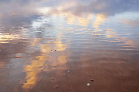 Sandy shore of the Baltic sea. Clear sunset sky, colorful glowing pink clouds, soft light. Symmetry reflections on water, natural mirror. Texture, background. Weather, winter, climate change, natureの写真素材