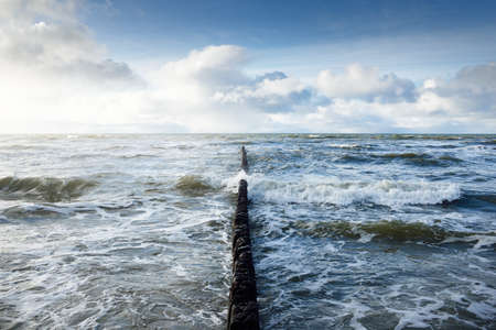 View of the Baltic sea from sandy shore (sand dunes). Clear sky, glowing clouds, sunbeams. Waves, water splashes. Old pier (jetty) for fishing boats. Idyllic seascape. Winter, climate, nature. Denmarkの写真素材