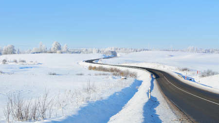 Panoramic view of the clean winding S shape highway through snow-covered field, forest, village. Winter rural scene. Travel, Christmas vacations, logistics, dangerous driving, off-road, transportationの写真素材